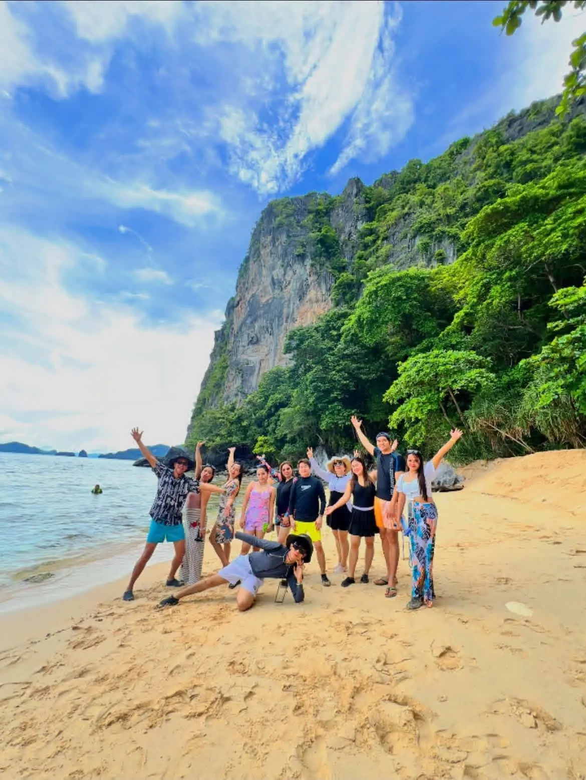 A tour group celebrating on a beach under a green cliff