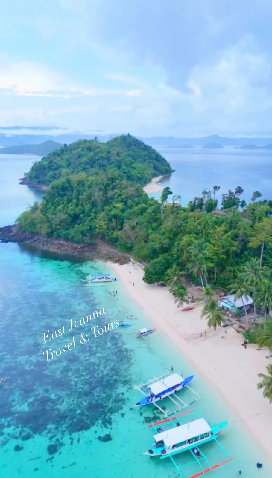 An island ringed by turquoise water with boats at its beach